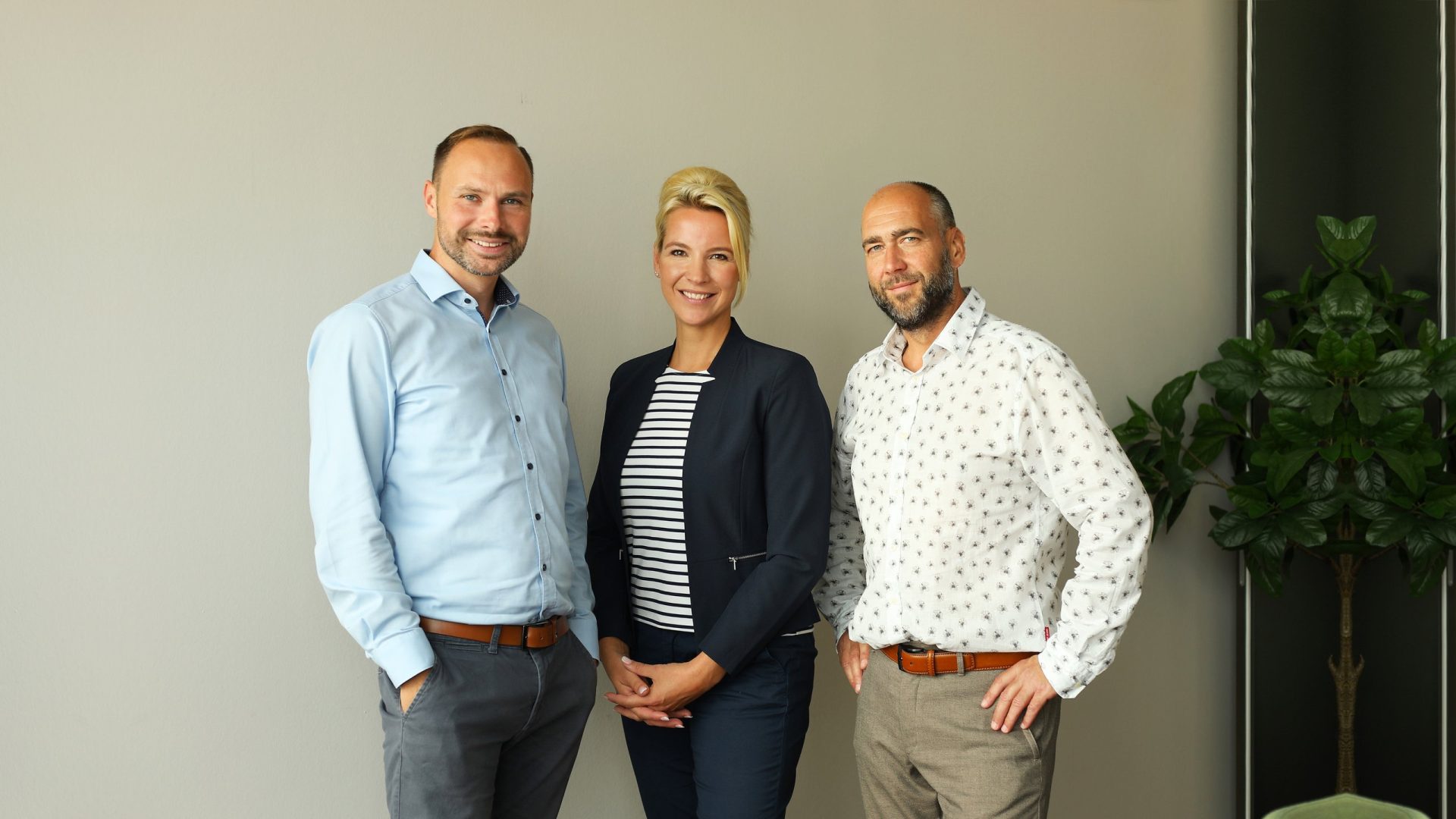 Drei Mitglieder des advandas-Teams stehen vor einer hellen Wand neben einer Zimmerpflanze